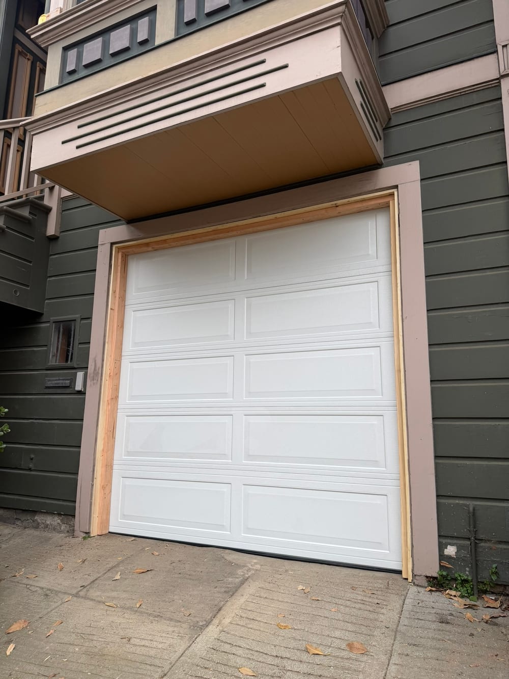 New white single-car garage door with fresh jamb trim under a bay window on an older wood-sided house