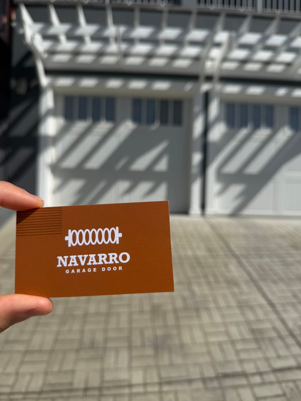 Navarro Garage Door business card held up in front of two carriage-style garage doors