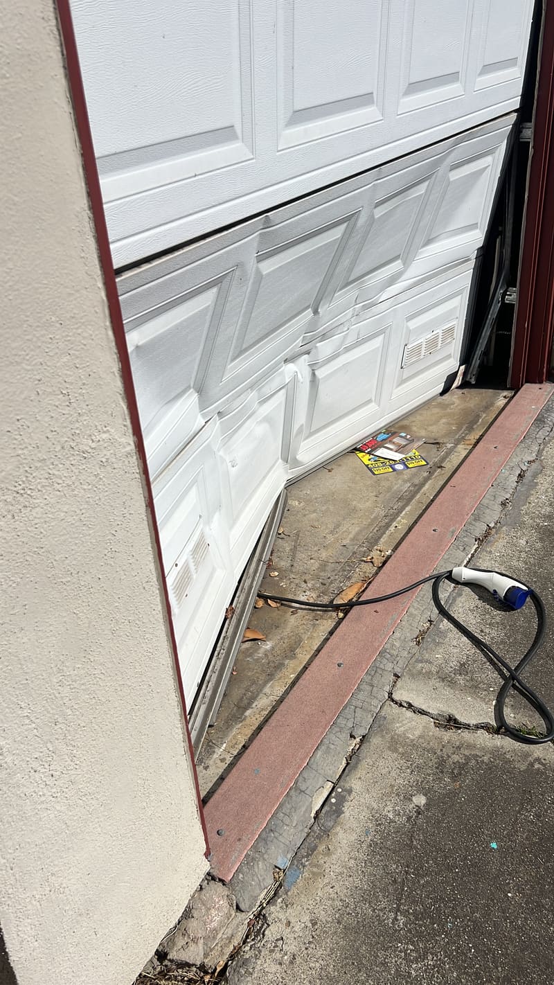 Garage door hanging crooked in its opening, one side lower than the other